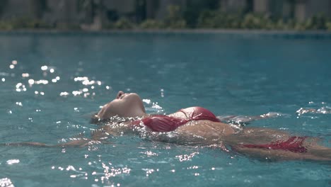 slim lady in trendy red bikini swims in crystal blue pool