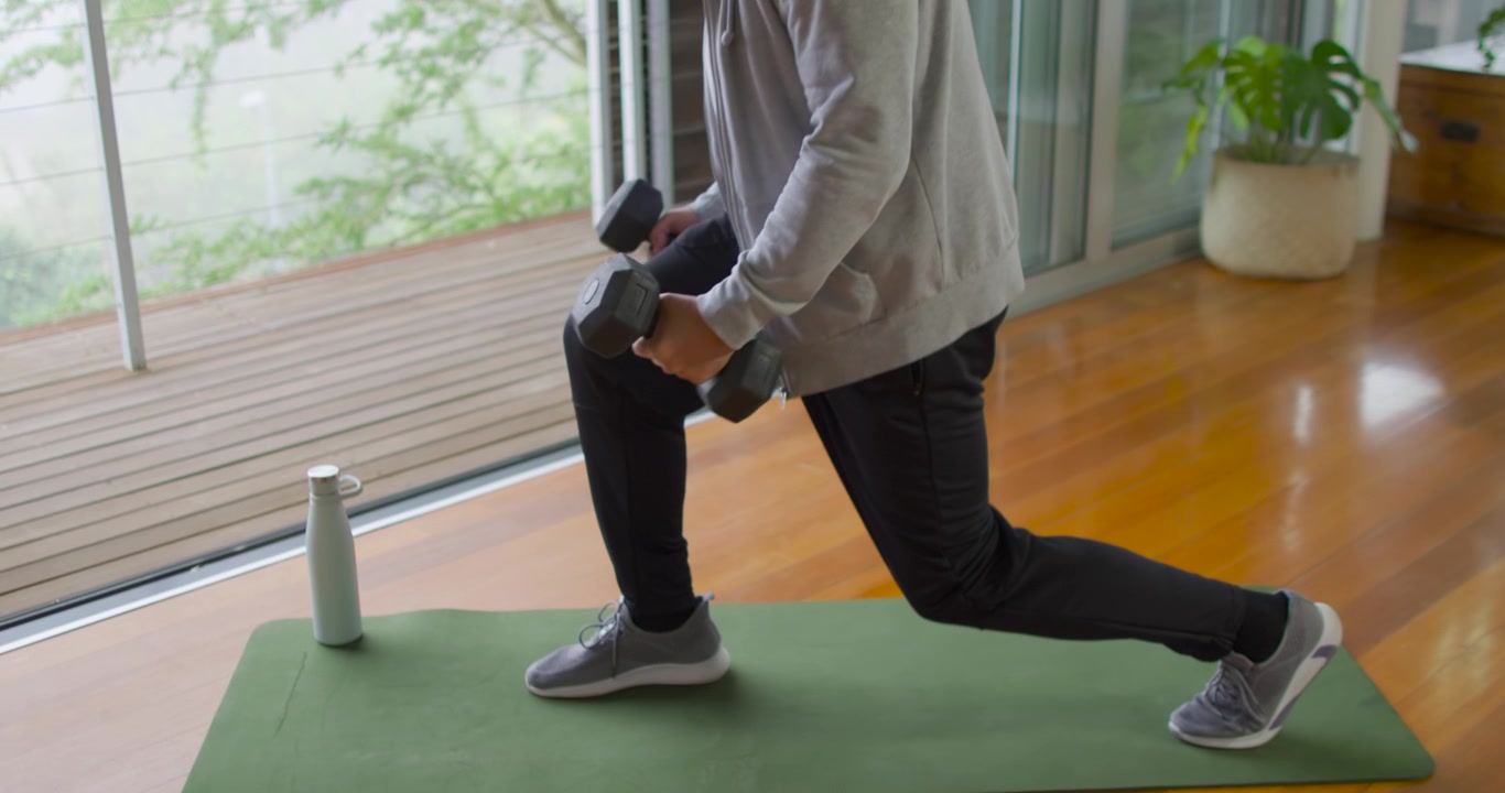 Senior Asian man starting deep lunge performing lunges on mat at home with dumbbells for strength
