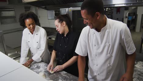 Diverse-group-of-chefs-preparing-dough-and-talking-in-restaurant-kitchen