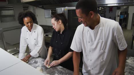grupo diverso de chefs preparando masa y hablando en la cocina del restaurante