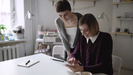 Two-woman-friends-looking-photo-in-social-network-by-tablet-pc