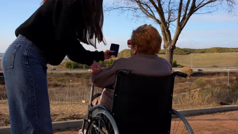 granddaughter teaching her wheelchair-bound grandmother how to use a cell phone