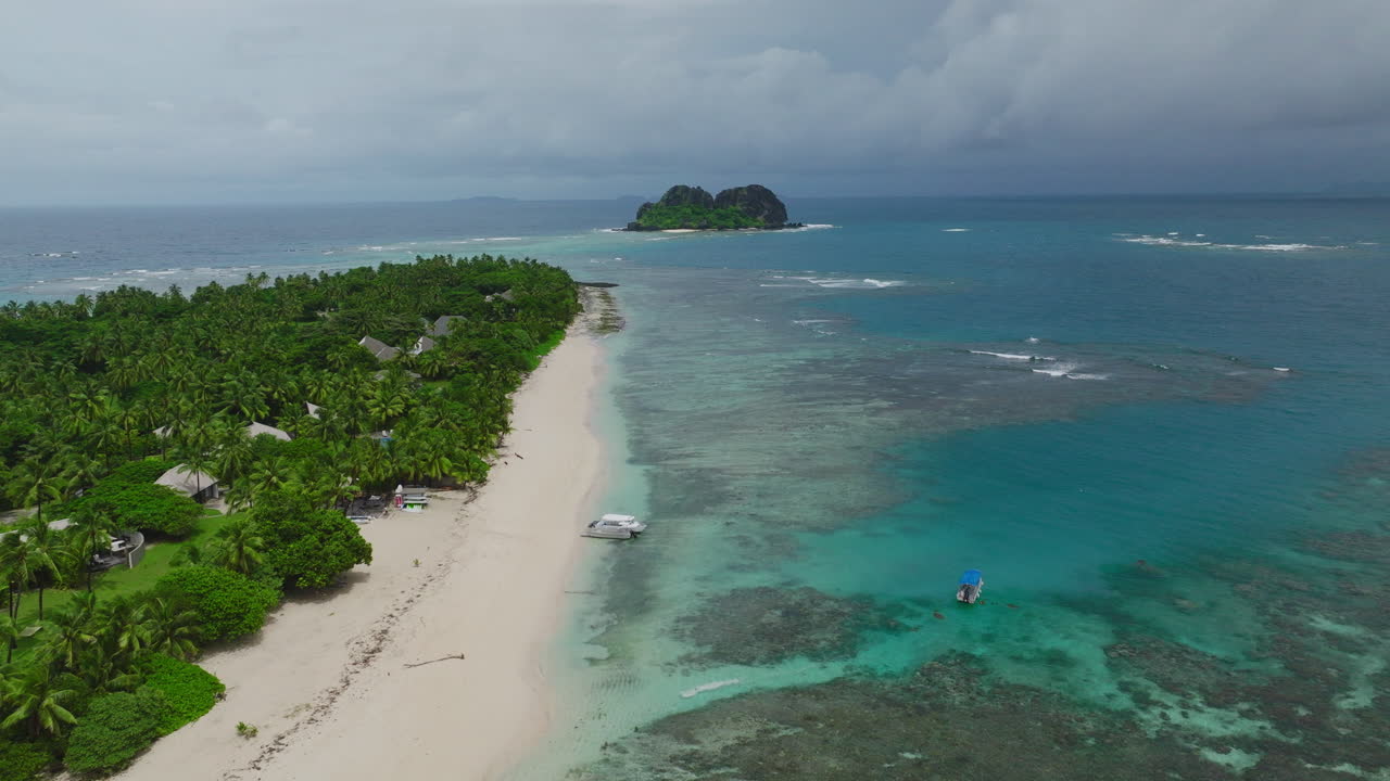 Drone of narrow sandy island lined with palm trees and turquoise sea