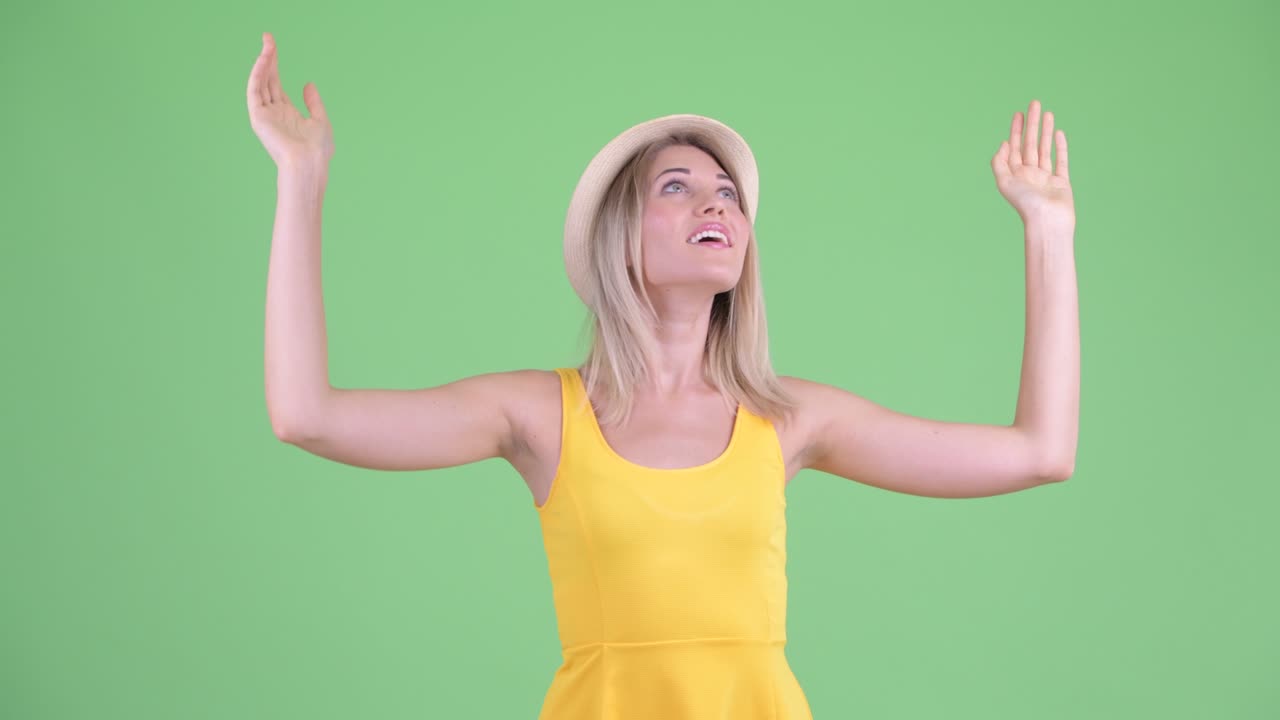fotografía de estudio de una joven turista mujer mirando emocionada al cielo como si algo fuera cayendo de allí contra un fondo verde