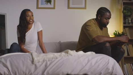 Young-Couple-At-Home-At-Night-In-Bedroom-With-Woman-Talking-To-Man-Scrolling-Internet-On-Mobile-Phone-2