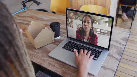 mujer tomando un bocadillo mientras hace una videollamada en una computadora portátil en una cafetería