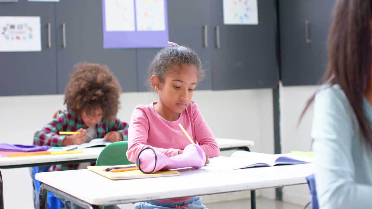 In school, girl writing in notebook at classroom desk, concentrating on work