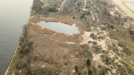 aerial top down shot of natural landscape with small lake bordering baltic sea in poland