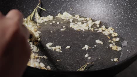 chef frying garlic with rosemary in oil on non-stick pan