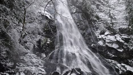 snow gently falls while orbiting slowly through a winter forest, cascading waterfall, aerial drone