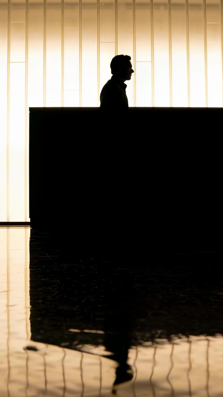 Vertical video: Entering suited man walking to counter in lobby lit wall shiny floor, copy space