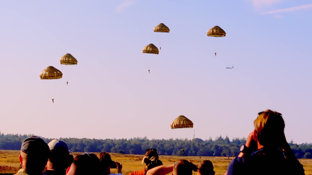 Group of parachutists descending in a synchronized formation against a clear sky at sunset during the Airborne Ede event at Ginkelse Heide, Netherlands. Beautiful lighting enhances the scene