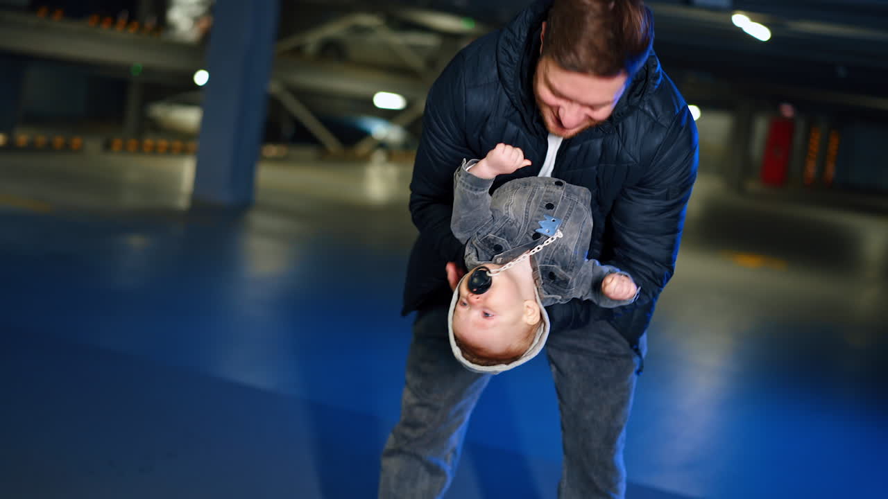 Man in black jacket holding a little baby. Happy dad plays with his beloved infant son.