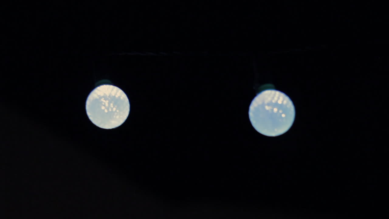 Blue globe string lights shimmer in the dark, casting a cool glow as the camera glides smoothly from left to right