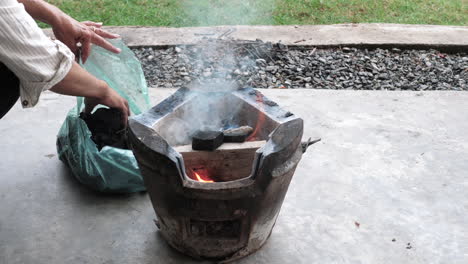 person adding charcoal to traditional thai clay stove hot fire - thailand food