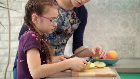 Mother-learning-daughter-to-use-knife.-Mom-and-child-cut-apple-slice-together