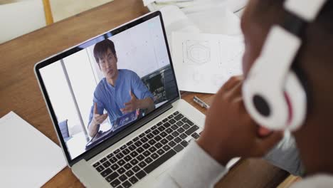 African-american-businessman-sitting-at-desk-using-laptop-having-video-call-with-male-colleague