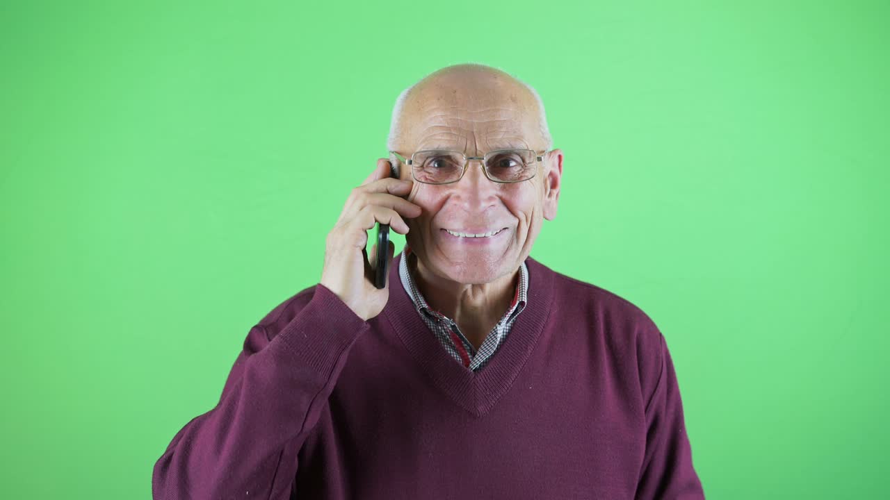 Studio portrait of aged man talking by phone isolated on green background