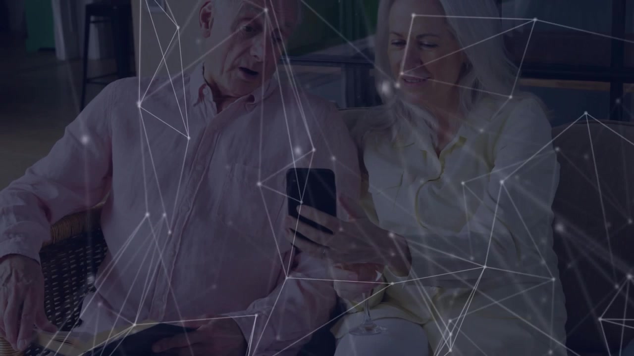 Dojrzała kobieta przechylająca smartfon w stronę mężczyzny z branży technologicznej, udostępniająca dane, podczas gdy nakładka unosi się na sofie.