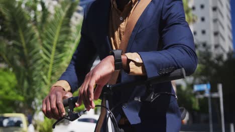 African-american-businessman-using-smartwatch-leaning-on-bike