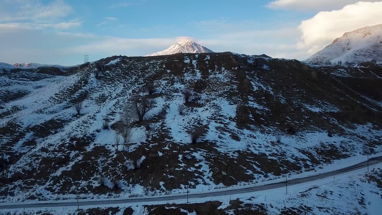 겨울의 추운 일출에 드론 촬영을 시작하여 마을 도로에서 다마반드 산 정상까지 구름이 가득한 푸른 바람이 부는 하늘의 아름다운 풍경 속에서 얼음과 눈으로 뒤덮인 풍경을 감상할 수 있습니다.