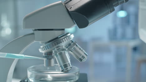 black scientist in protective wear examining chemical through microscope