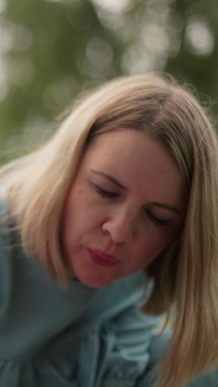 se ve a una mujer con un vestido azul soplando aire en algo atentamente mientras que una vista borrosa de un niño con gafas aparece en el fondo