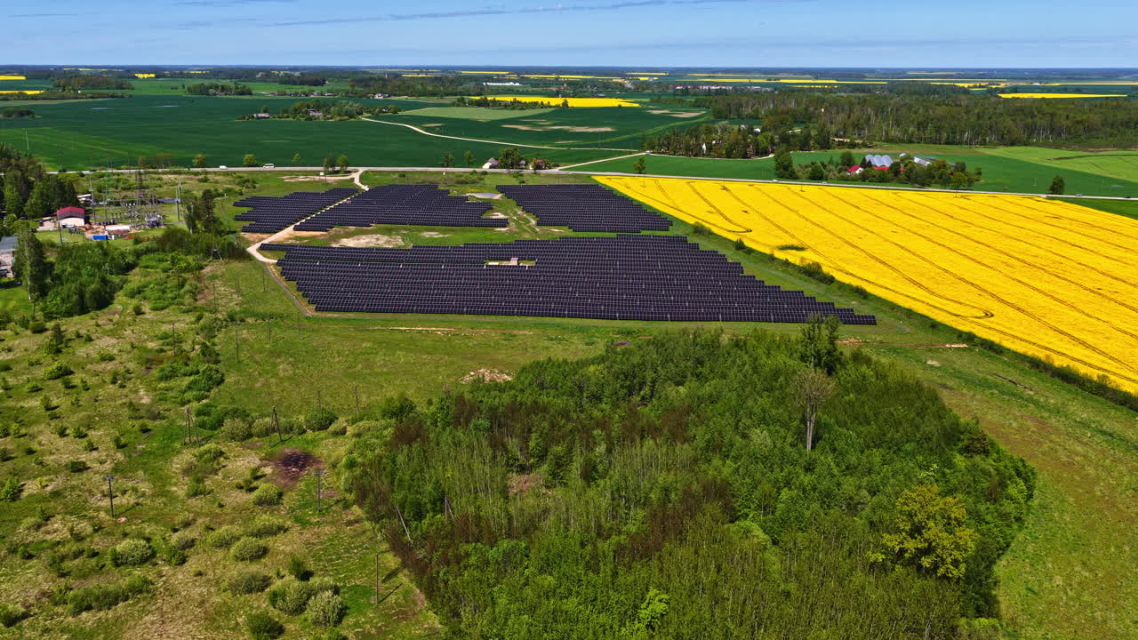 Aerial view of solar energy farm between yellow rapeseed and green fields