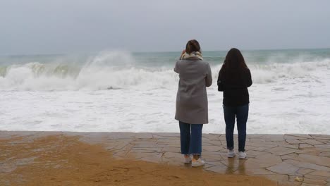 two people from the back watching the big waves break on the costa brava