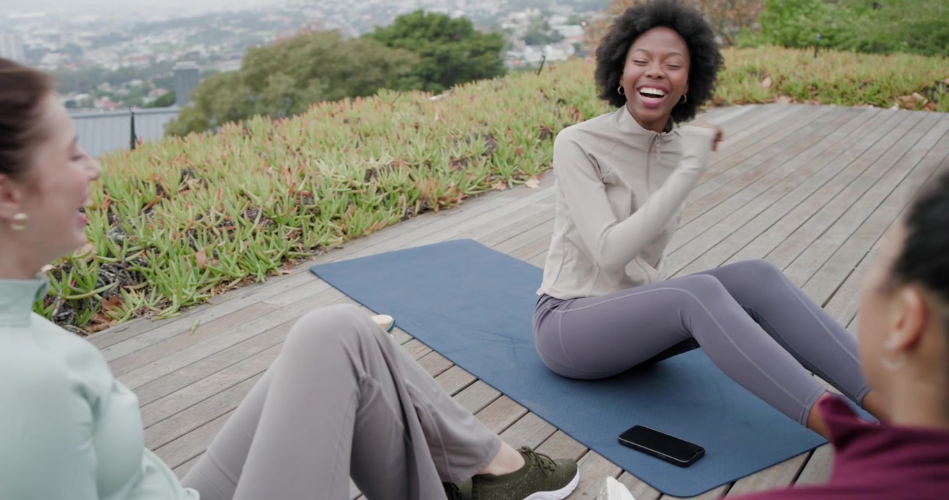Forskellige kvinder sidder på tagterrasse efter yoga, afroamerikansk kvinde leder samtale, telefon på blå måtte