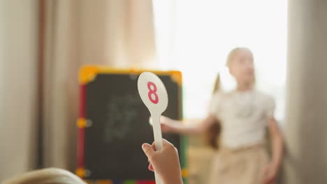 Toddler-boy-shows-answer-on-tag-girl-writes-on-blackboard