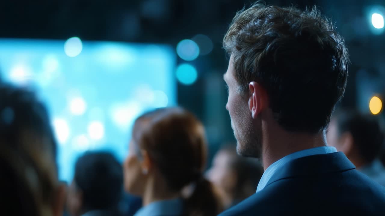 Un uomo in abito guarda una presentazione. Folle si radunano, attenzione concentrata. Luci blu brillano sullo sfondo. Ideale per eventi aziendali o conferenze. Evoca coinvolgimento professionale e interesse.