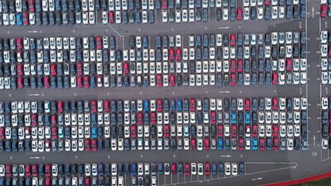 aerial zoom out revealing vast parking lot filled with rows of new imported vehicles awaiting distribution, showcasing automotive industry logistics and port operations