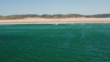 Aerial:-Surfing-the-beach-of-Bordeira-in-the-Algarve,-Portugal