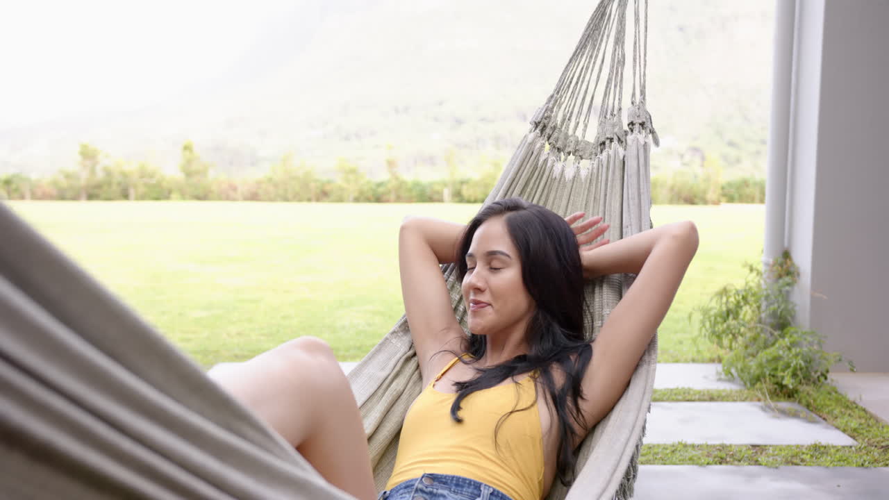 A young biracial woman relaxes in hammock, hands behind her head