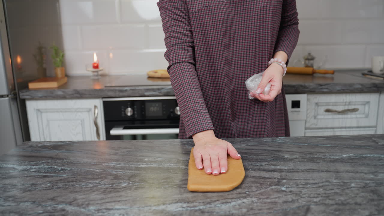 타일로 된 주방 벽, 롤링 핀, 그리고 은 불을 배경으로 카운터에 반죽에 손을 넣는 동안 접힌 색 을 들고 있는 칠색 드레스를 입은 여성