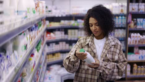 Black-woman-doing-grocery-shopping-in-supermarket,-looking-at-full-shelves-buying-food