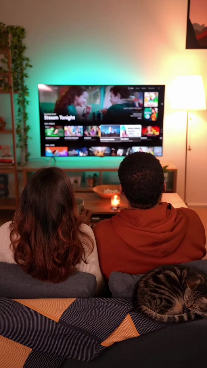 Coppia e gatto che si rilassano sul divano guardando la TV in un accogliente soggiorno