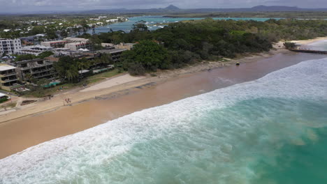 Toma-Aérea-De-La-Playa-De-Noosa-Con-Buggy-Salvavidas-Y-Caminantes-Y-El-Mar-Rodando