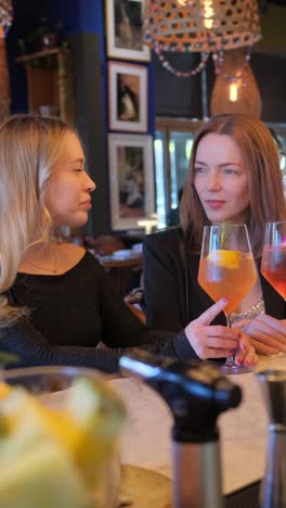 two women at a table in a restaurant holding wine glasses. two women are seated indoors at a restaurant, each holding a glass of wine. the scene is filled with a lively atmosphere, portraying a sense of fun and enjoyment