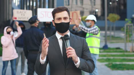 caucasian journalist or correspondent wearing protective mask giving interview in a protest against covid 19