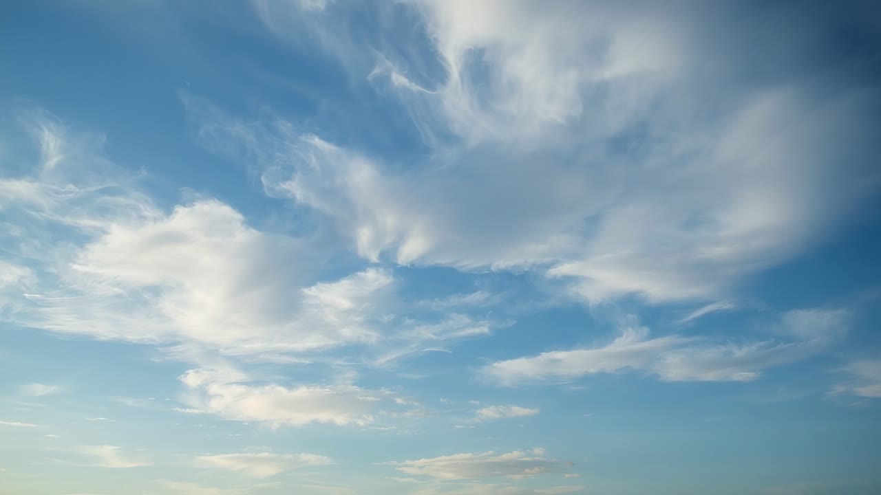 Drifting cloud cluster driven by wind aloft stretching reshaping over blue sky with horizon band