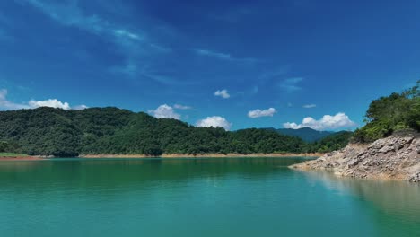 low altitude flight over natural lake named feicui reservoir with green jungle hills , sandy shore and blue sky