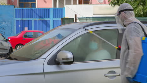 man in coverall spraying car with sanitations solution