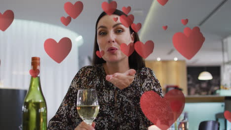 animation of hearts over caucasian woman drinking wine and having video call