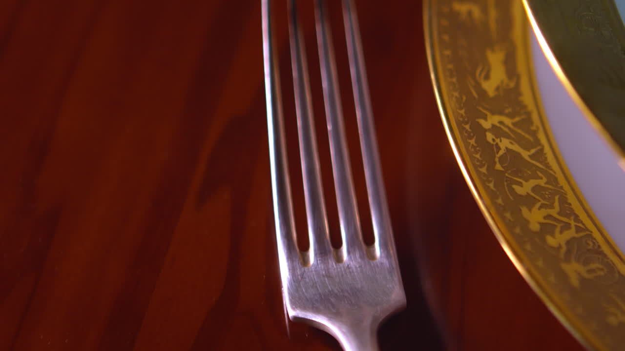 Dettagliata ripresa in tracking rivela posate d'argento e una ciotola placcata in oro su un tavolo da pranzo di lusso. Adatto per il branding di ristoranti premium e temi per eventi eleganti.
