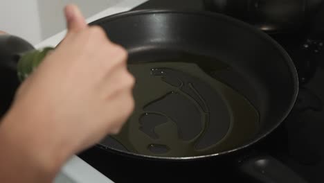 joven mujer marrón vertiendo aceite de oliva en una sartén en la estufa y cerrando la botella