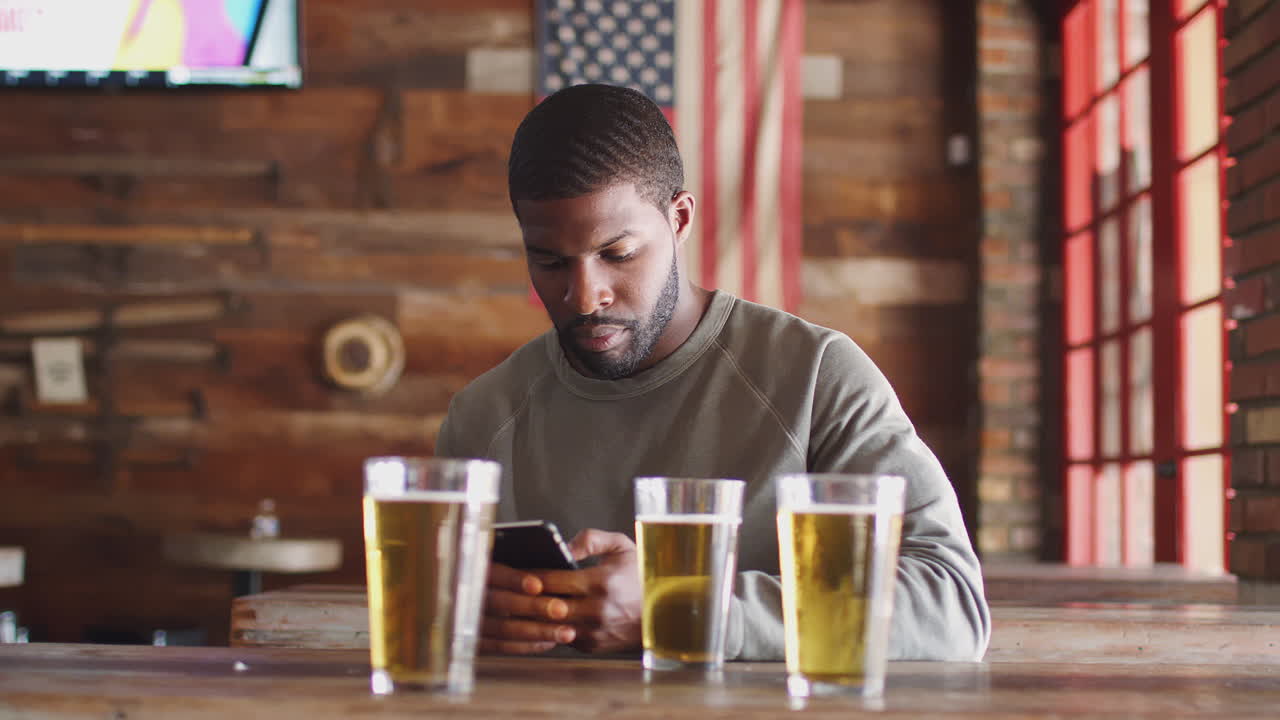 Man Sitting In Sports Bar Drinking Beer And Looking At Mobile Phone