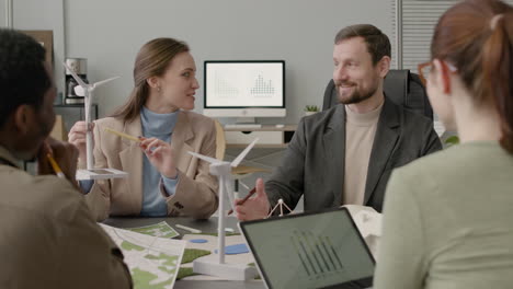 woman explaining wind turbine model and discussing about renewable energy project with her colleagues in the office