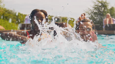 family having fun splashing with daughter in pool on summer holiday